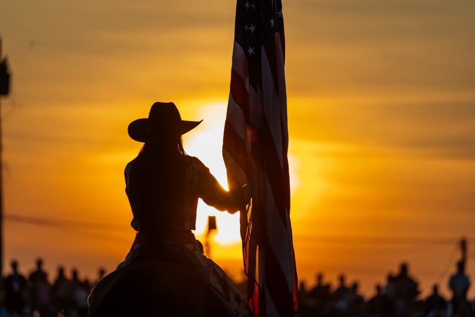 Kaycee carrying the American flag on horseback at dusk
